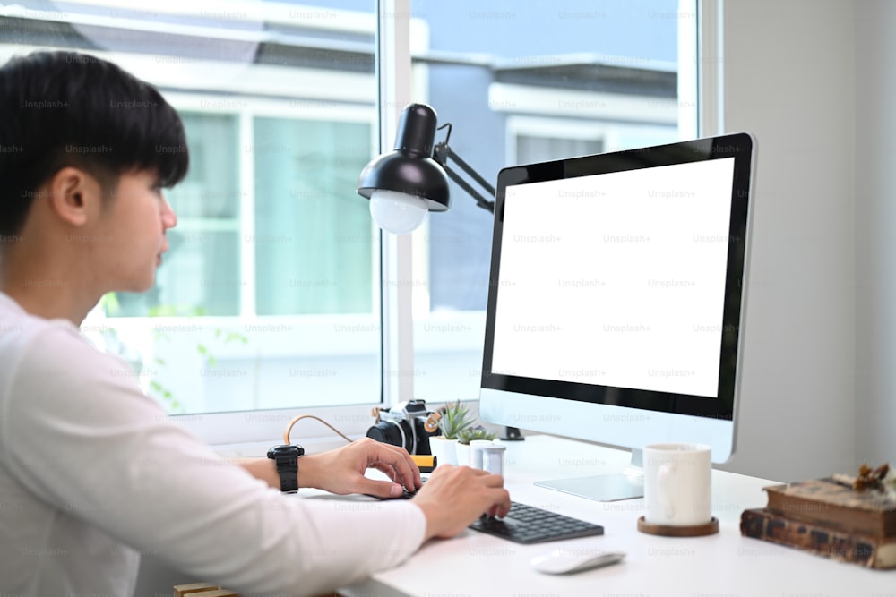 Side view of young man working on computer with white screen at home office.