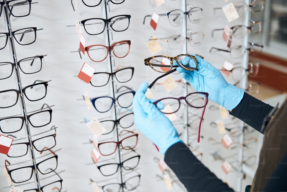 Cropped photo of a qualified female optometrist holding two pairs of fashionable glasses in her hands