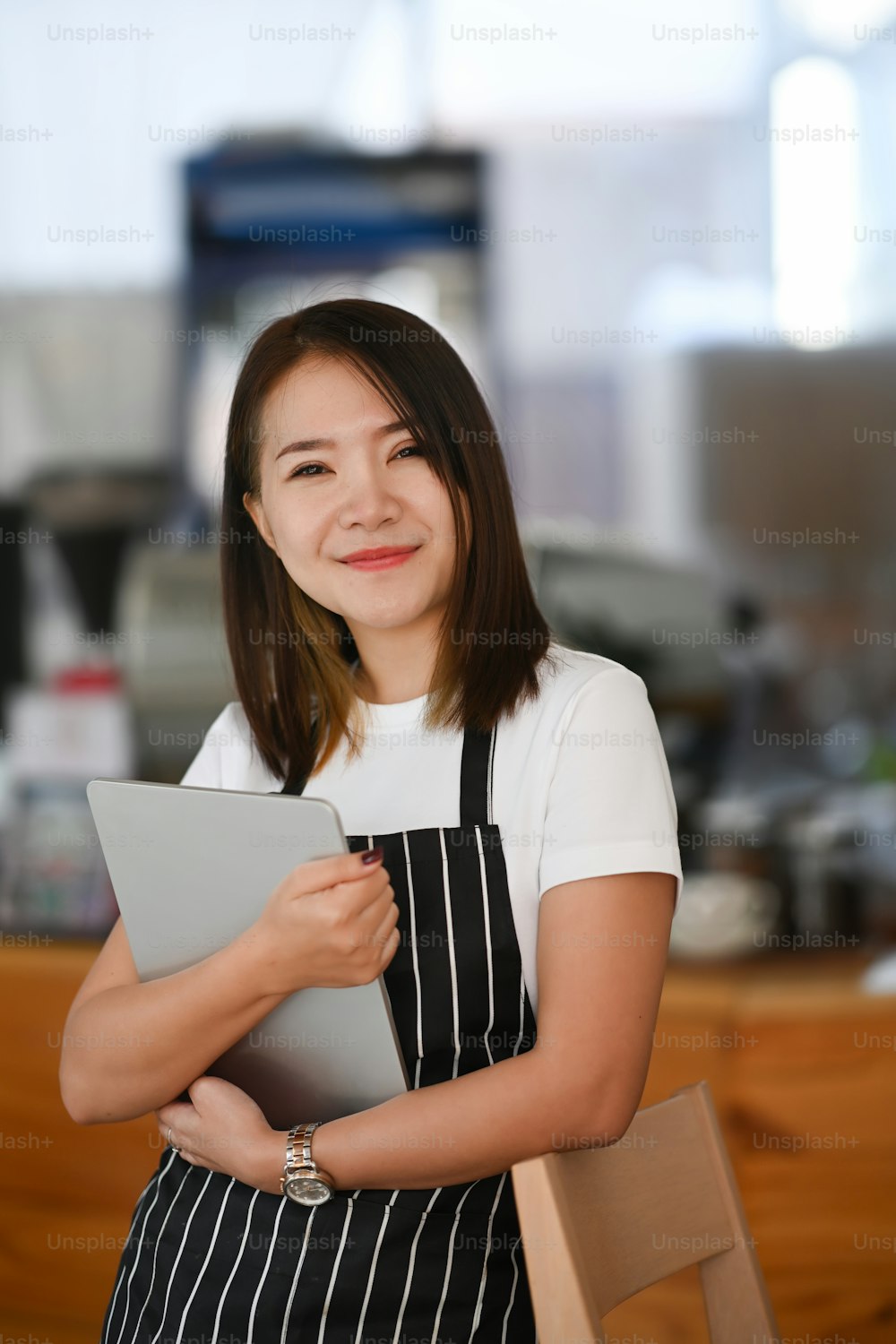 Porträt einer lächelnden Unternehmerin, die in ihrem Café steht und ein digitales Tablet in der Hand hält.
