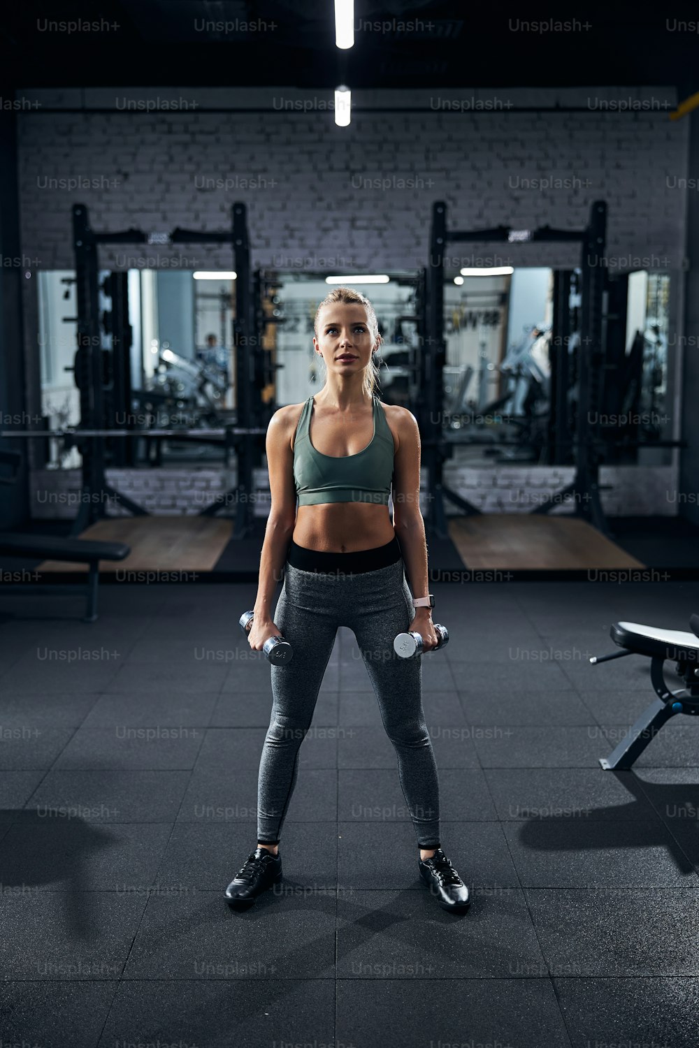 Sportsperson holding a dumbbell in each hand while standing on a black gym carpet