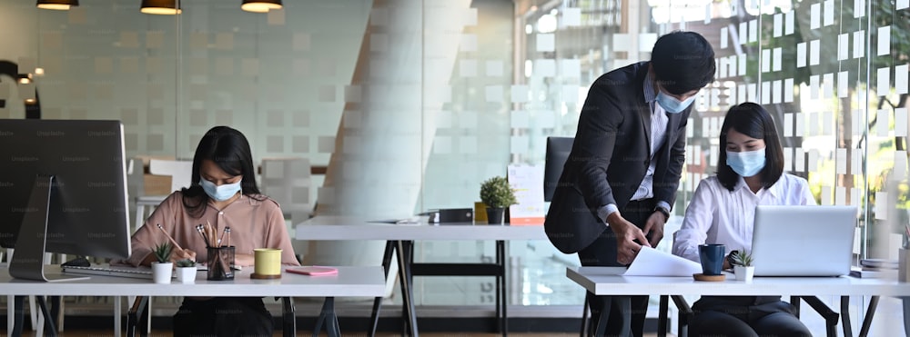 Horizontal image of businesspeople or office worker wearing medical mask while working in modern office.