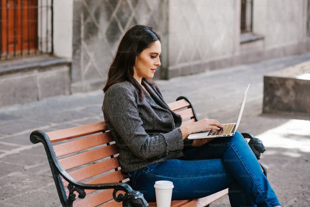 mexican woman working with her laptop in a park bench in a colonial city in Latin America