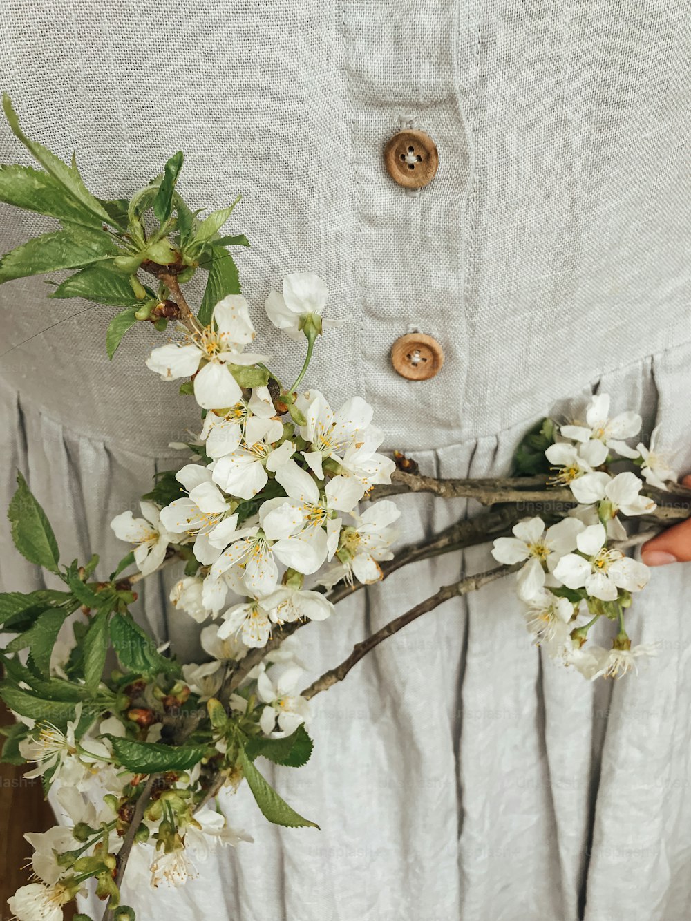 Mujer con vestido de lino rústico sosteniendo ramas de cerezo y manzana en flor. ¡Hola primavera y Felices Pascuas! Imagen estética simple. Flores de primavera en las manos