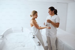 Waist up portrait of blonde Caucasian patient and dark hair worker talking together while looking to each other in room indoors
