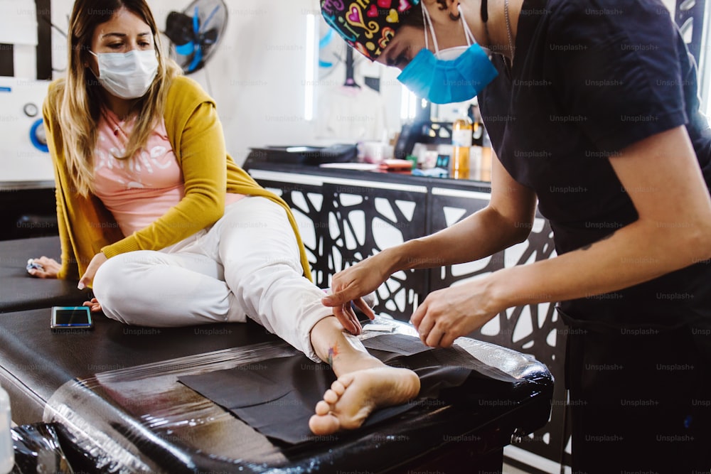 Latin woman tattoo artist demonstrates the process of getting tattoo with paint and works in blue sterile gloves in Mexico city