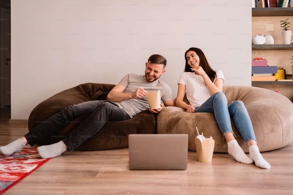 La feliz pareja disfruta del tiempo juntos mientras comen juntos y ven una película en la computadora portátil