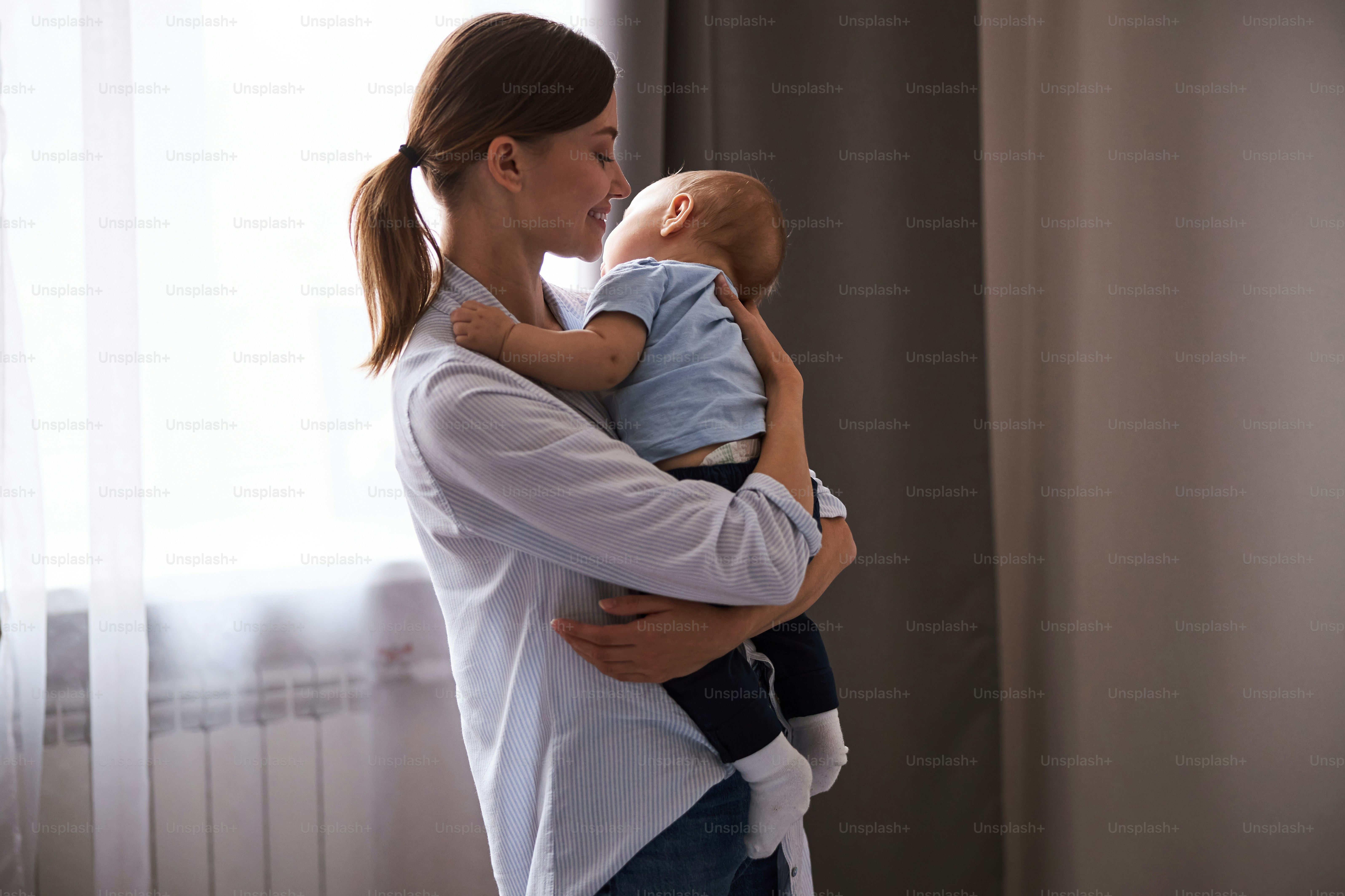Cheerful female person keeping smile on her face while holding her son in warm hugs