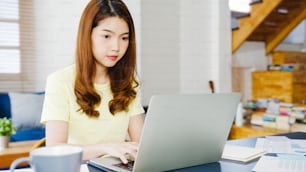 Portrait of freelance Asia women casual wear using laptop working in living room at home. Working from home, remotely work, self isolation, social distancing, quarantine for corona virus prevention.