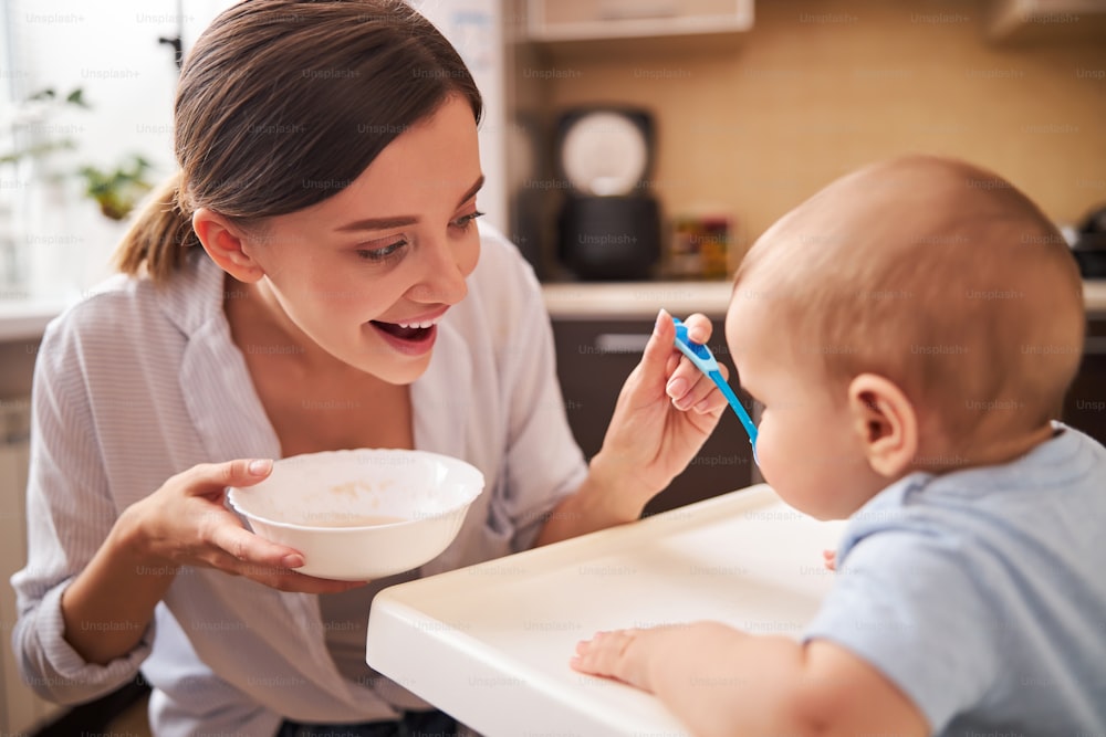 Attractive brunette woman keeping smile on her face while taking care of her child
