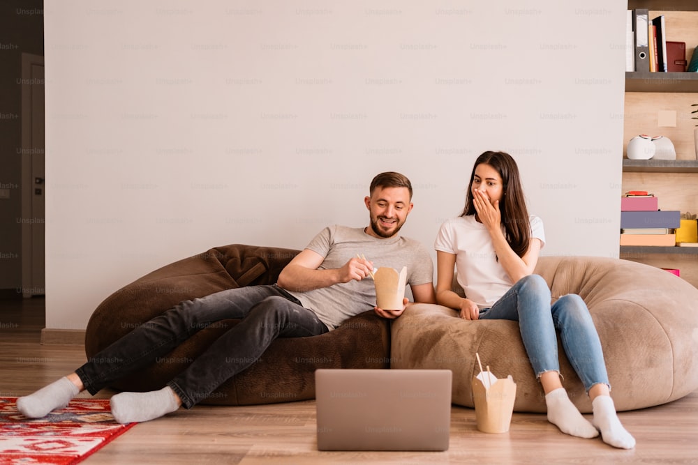 Glückliches Paar genießt die Zeit zusammen, während es zusammen isst und einen Film auf dem Laptop schaut