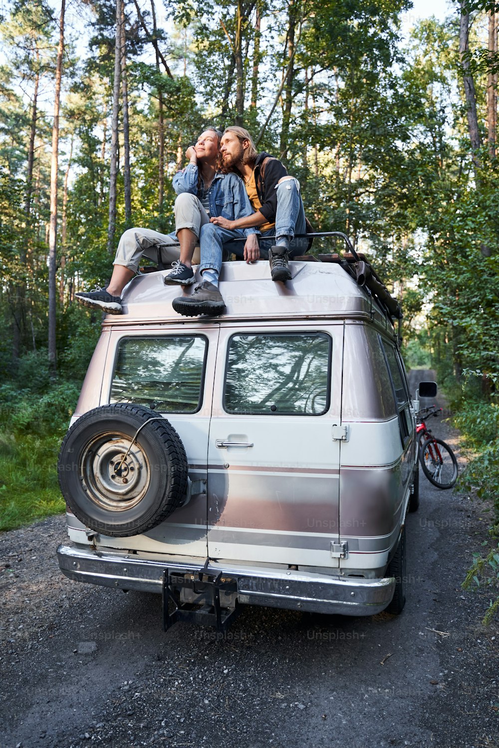 Loving couple sitting at the roof of a car in forest and enjoying a nature. Smiling man and woman together on camping trip