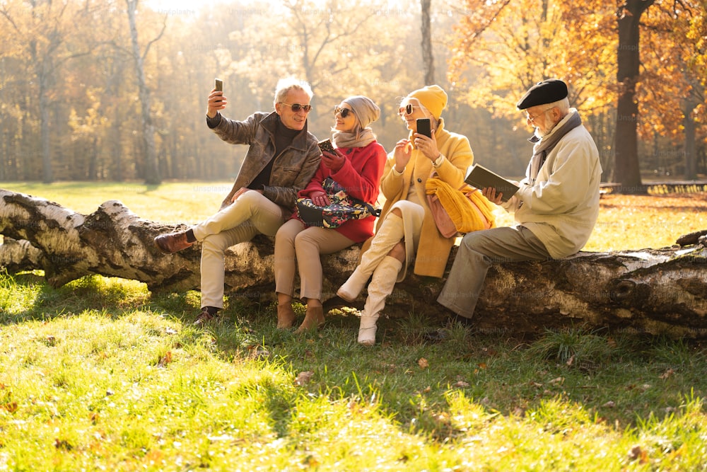 Senioren mit mobilen Smartphones im schönen Herbstpark. Ein älterer Mann liest ein Buch. Freunde im Ruhestand, die Zeit im Freien miteinander verbringen.