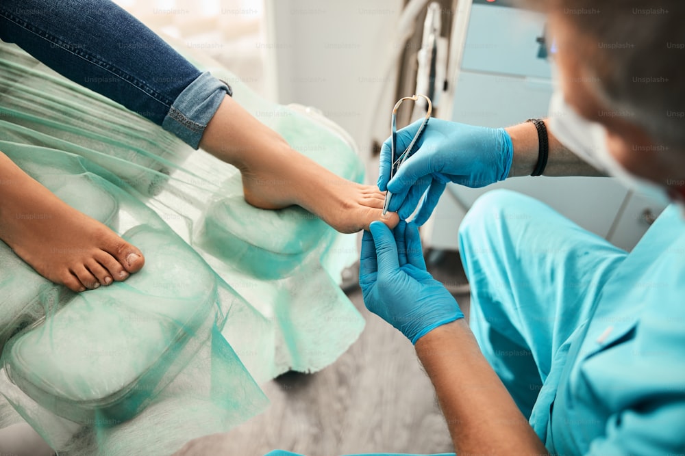 Retrato de vista lateral de las piernas femeninas en la silla médica mientras el médico podólogo trata la uña encarnada en la clínica de belleza