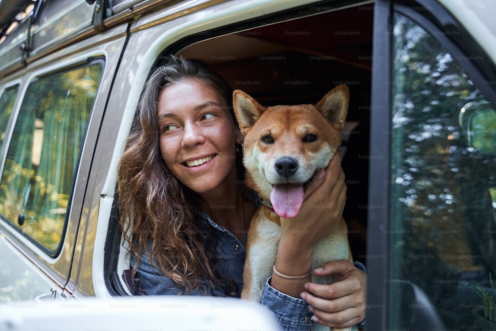 Eu sou amante de cães. Retrato do rosto da jovem menina bonita abraçando um cão energético fofo enquanto anda no carro ao redor das árvores ao ar livre