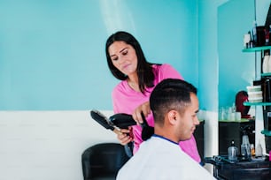 Professional hairdresser latin woman cutting hair with clipper machine and comb to a mexican man who gets haircut in Mexico city