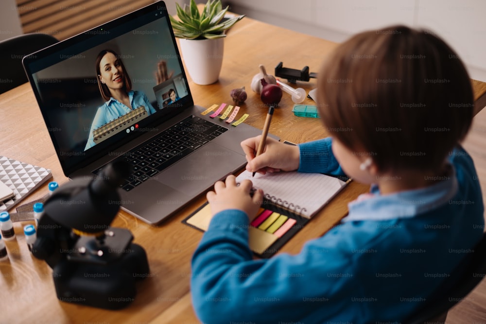 A Preteen boy uses a laptop to make a video call with his teacher. The Screen shows an online lecture with a teacher explaining the subject from class.