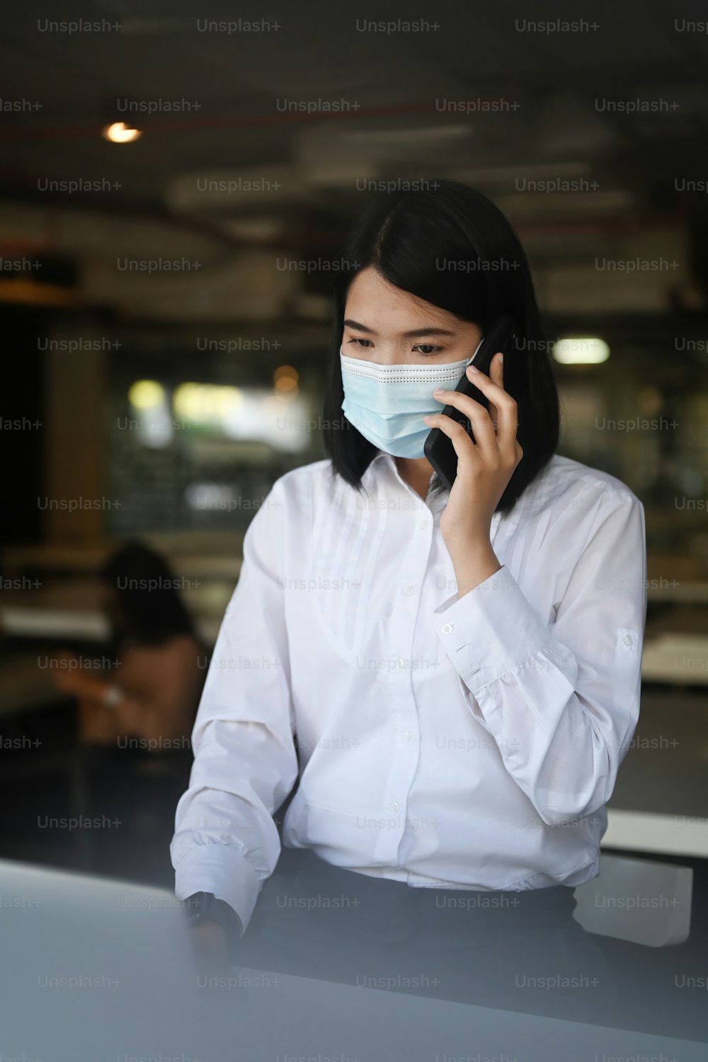 Portrait of businesswoman wearing face mask sitting in modern office and talking on mobile phone.