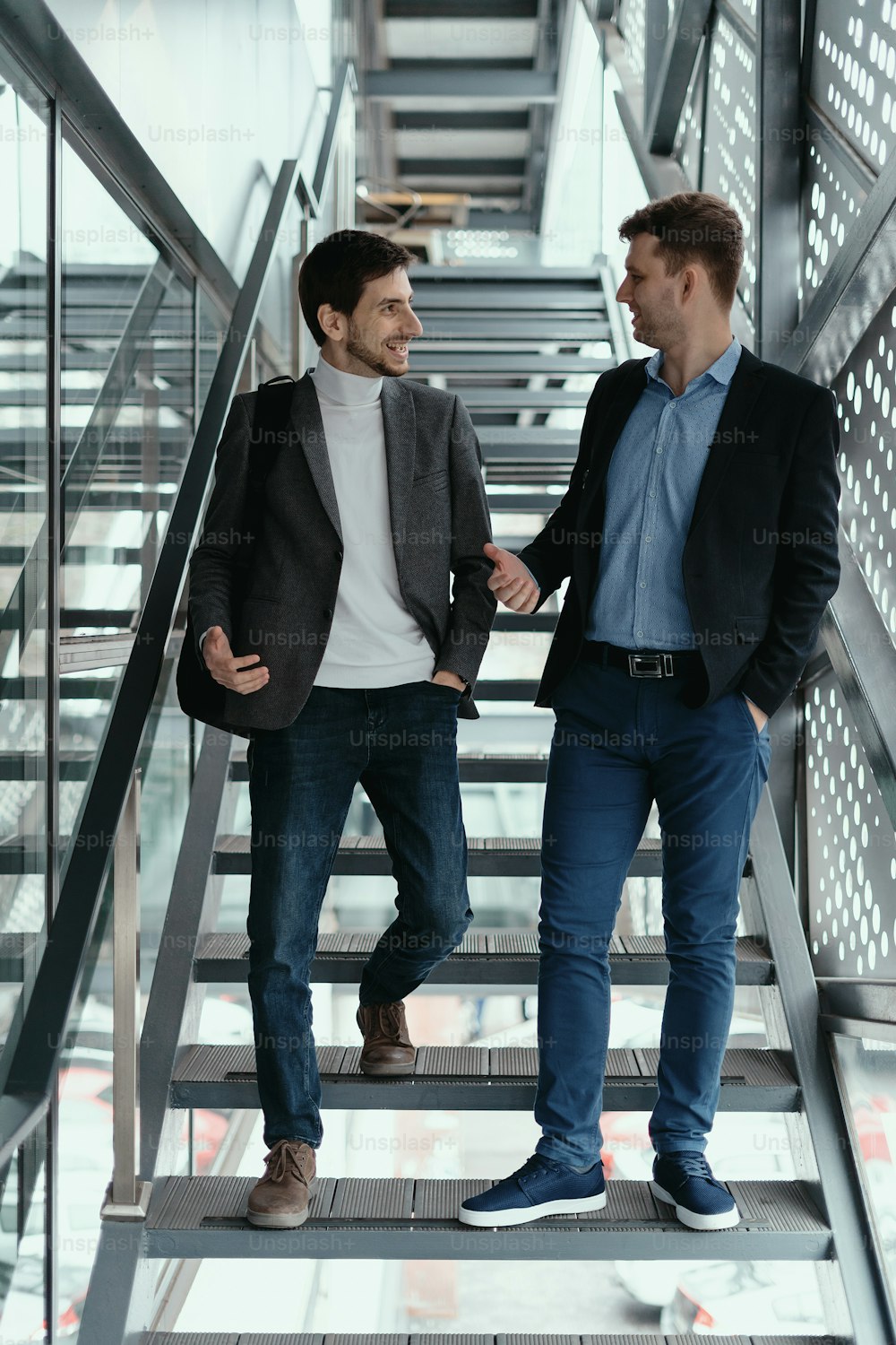 Two young businessmen going up, down the stairs while chatting in a modern building.