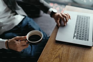 사업가는 미래 배경에 커피 한 잔을 들고 노트북으로 작업하고 있다. 밀레니엄 기업가 개념.