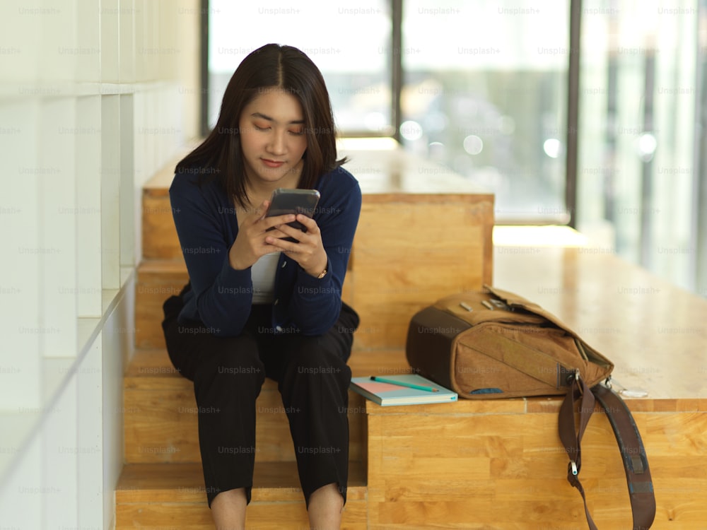 Portrait of female university student using smartphone while relaxed sitting in co working space