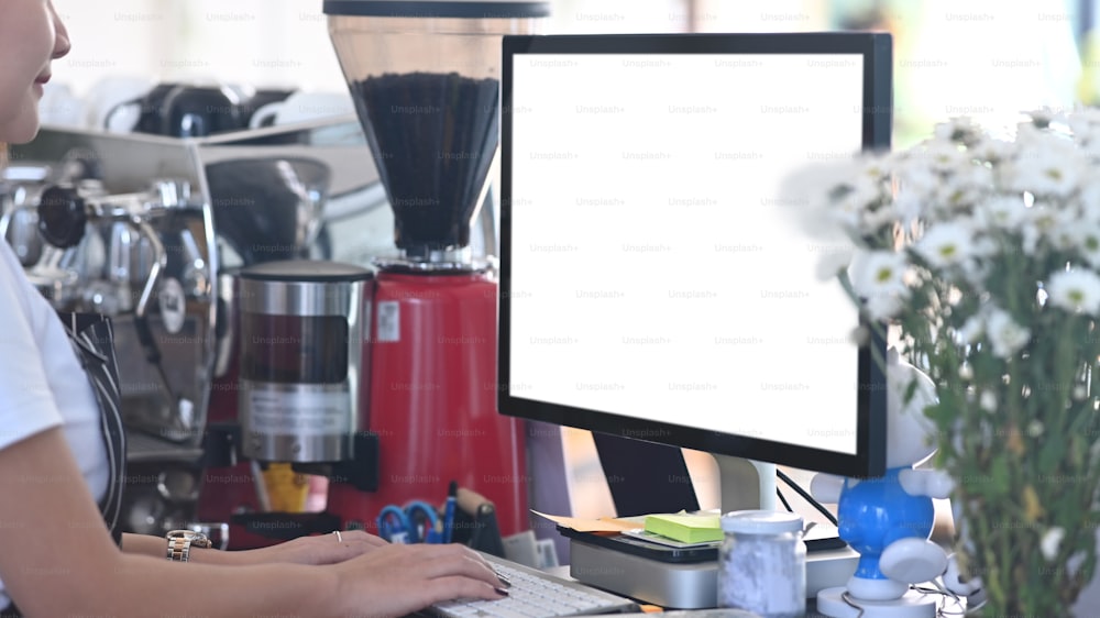 Close up view of barista waitress using computer on counter bar to check stock in coffee shop.