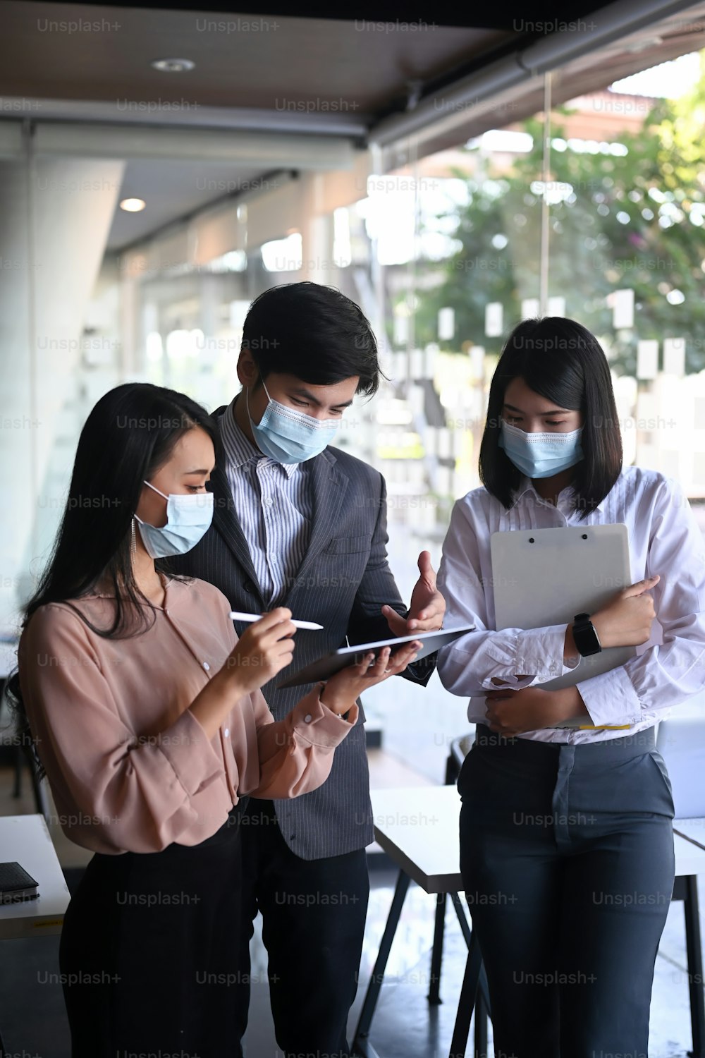 Des hommes d’affaires portant un masque de protection à l’aide d’une tablette numérique et discutant de la stratégie pour les affaires tout en étant debout au bureau.