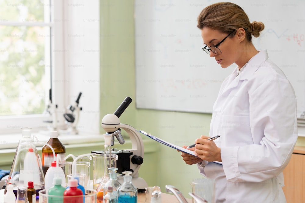Jeune femme scientifique rédigeant un rapport dans un laboratoire lors d’un travail de recherche