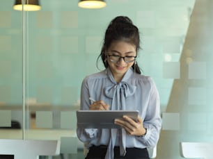 Portrait of businesswoman working with digital tablet while standing in glass partition office room