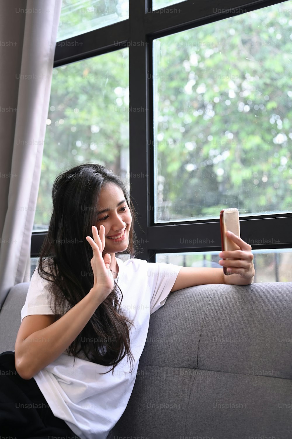 Portrait of confident lady holding smart phone making selfies while sitting on sofa at home.