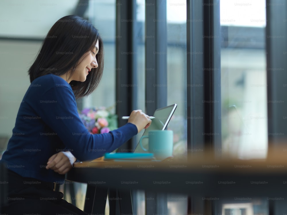 Side view of female student doing assignment with tablet on wooden bar in cafe