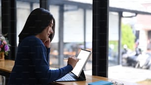 Side view young female designer working with tablet computer while sitting by the window.