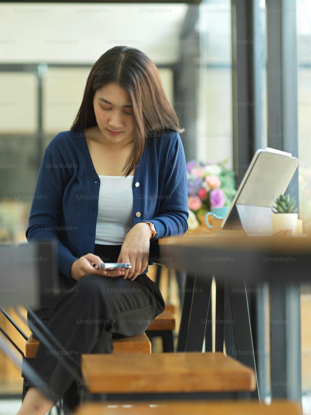 Retrato do estudante universitário feminino que usa o smartphone enquanto está sentado no bar de madeira no café