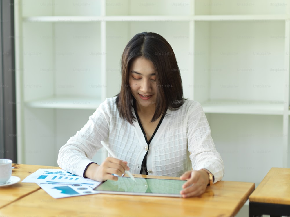 Porträt einer Geschäftsfrau, die mit einem digitalen Tablet auf einem Holztisch im Büroraum arbeitet