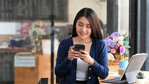 Cheerful young female freelance working in modern cafe and using mobile phone.