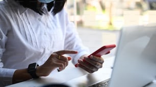 Close up view businesswoman sitting in front of laptop computer and using mobile phone at her workspace.