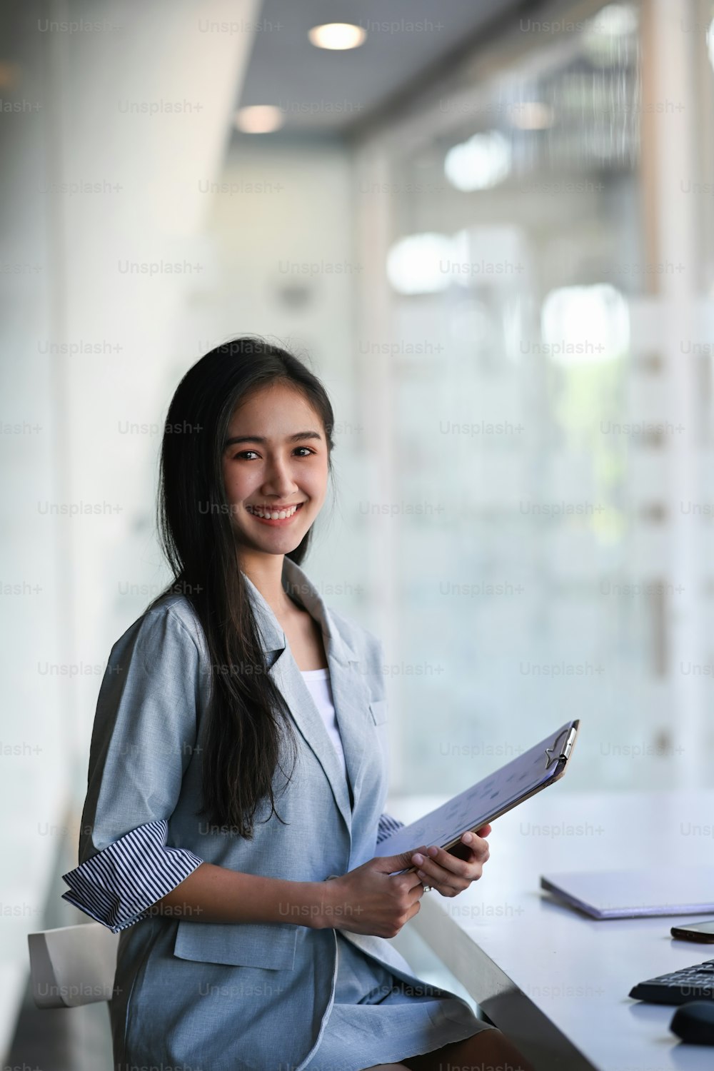 Portrait of confident businesswoman holding a document and smiling to camera while sitting in modern office.