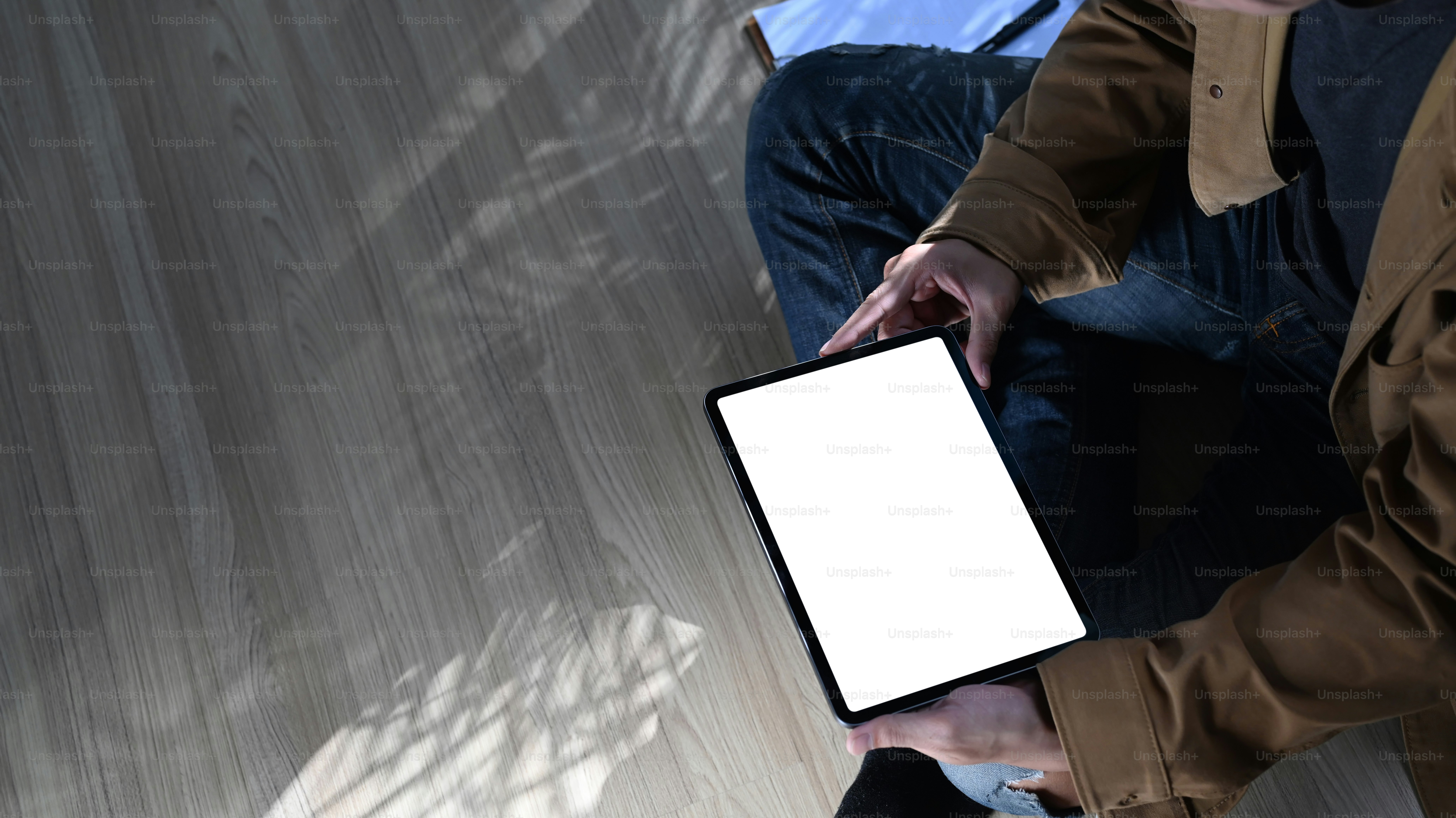Cropped shot of young man freelance sitting on wooden floor and using digital tablet.