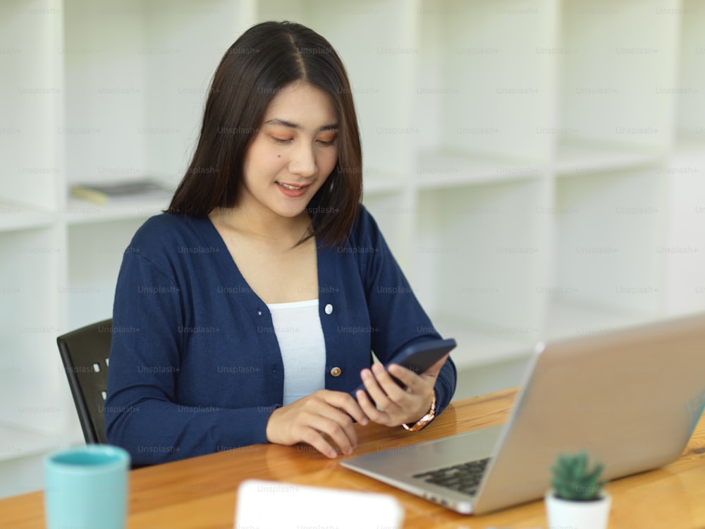 Porträt einer Geschäftsfrau, die mit Smartphone und Laptop auf dem Arbeitstisch im Büroraum arbeitet