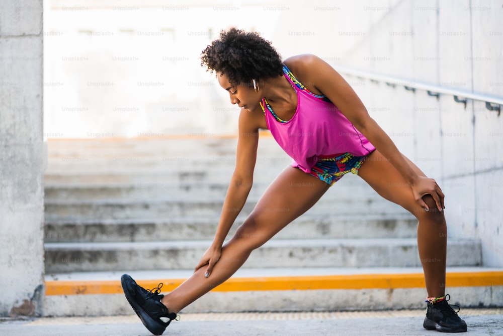 Retrato da mulher atleta afro esticando as pernas antes do exercício ao ar livre. Desporto e estilo de vida saudável.