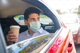 Portrait of businessman wearing face mask and drinking coffee in car on way to work. New normal lifestyle concept. Business concept.
