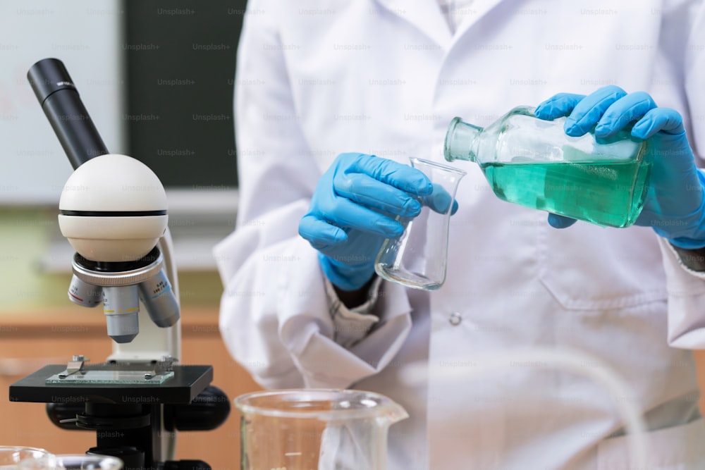 Wissenschaftler gießt während der Forschungsarbeit in einem Labor Substanz von einem Kolben in einen anderen