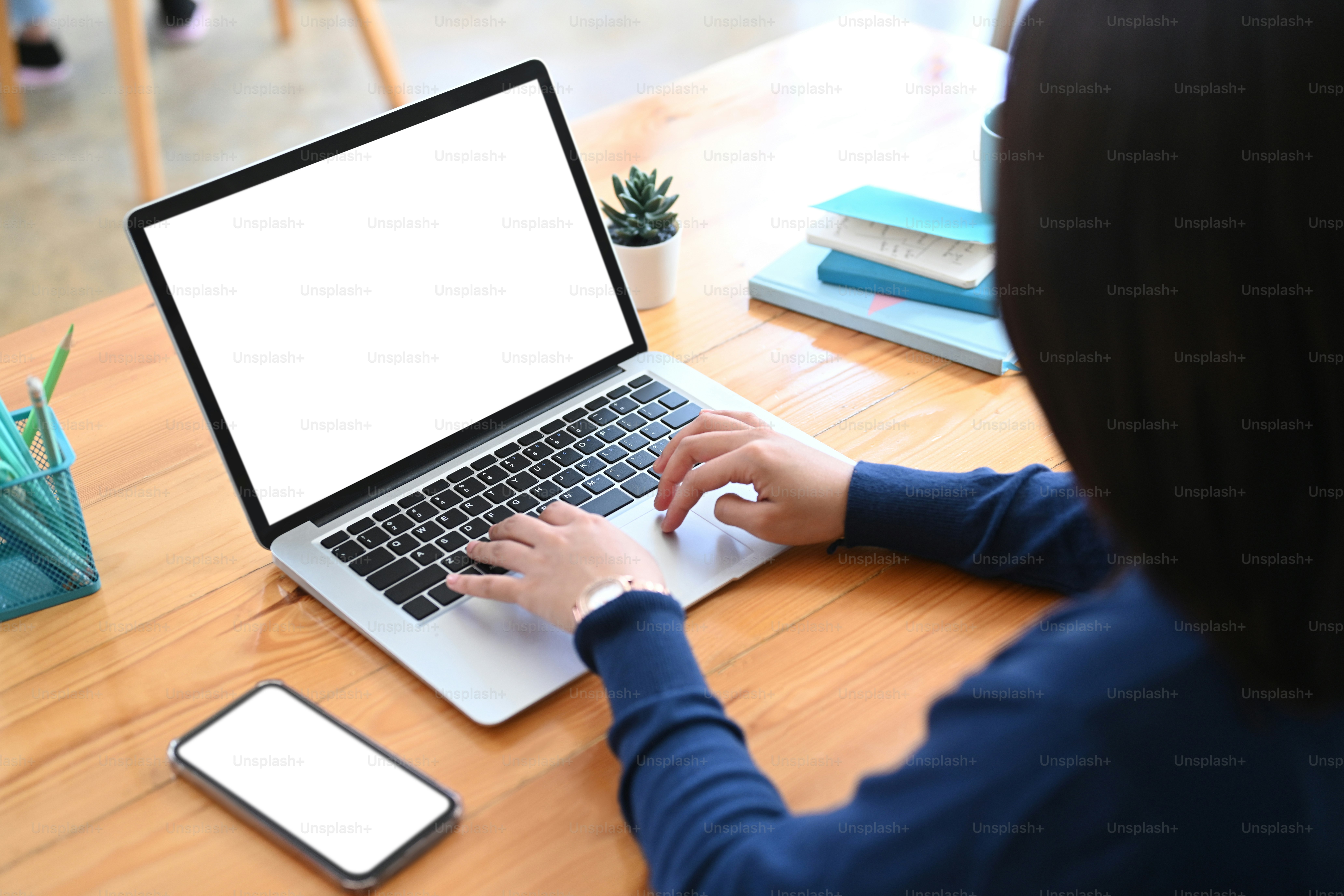 Tampilan belakang pekerja lepas wanita yang bekerja dengan komputer laptop di atas meja kayu.