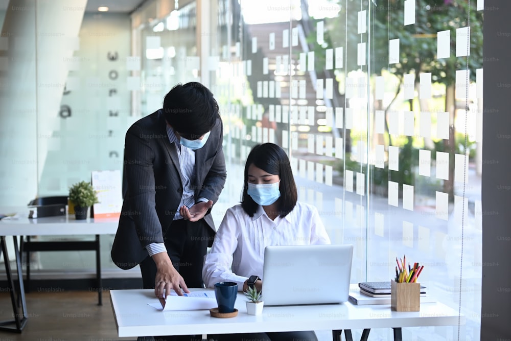 Business meeting of two partners wearing protective mask working together and discussing strategy for company growth in office.