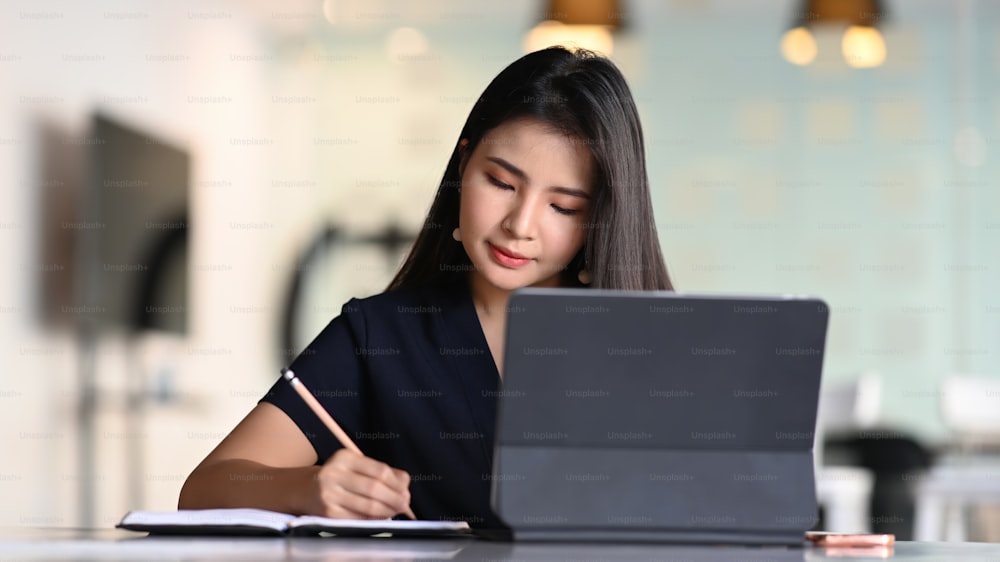 Businesswoman working with tablet computer and concentrate writing in formation on notebook.