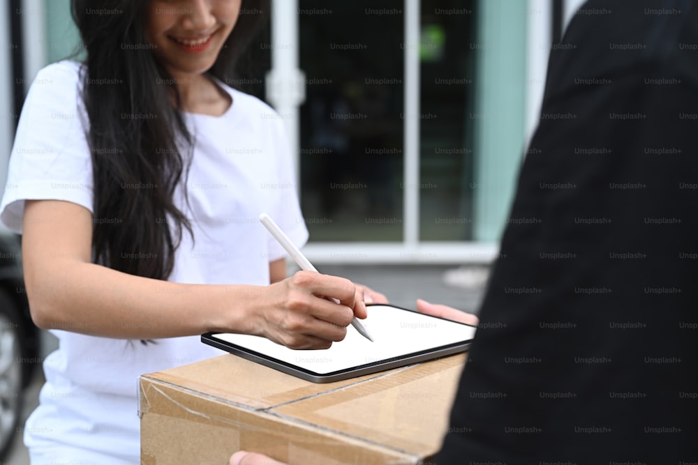 Cropped shot of young woman signing on digital tablet receipt of delivery package from delivery man.