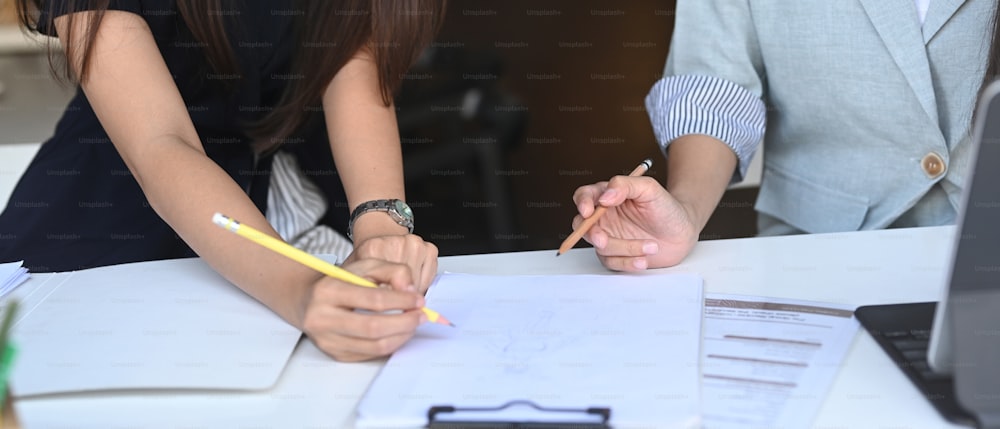 Cropped shot of two businesswoman analyzing documents on office desk.