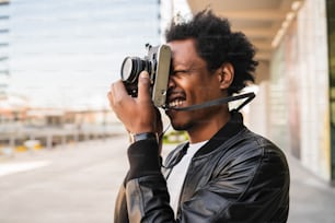 Porträt eines Afro-Touristen, der mit der Kamera fotografiert, während er im Freien auf der Straße spazieren geht. Tourismuskonzept.