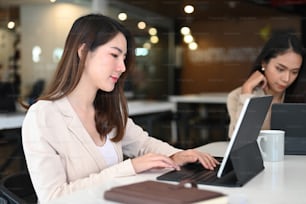 Two young businesswoman using tablet computer and working together in office.