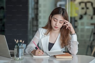 Retrato de una joven empresaria asiática cansada sentada en la mesa con una computadora portátil en la oficina.