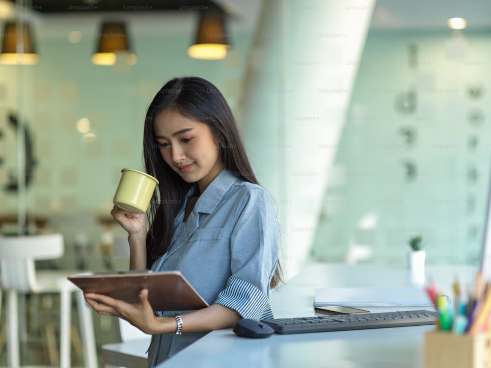 Side view of businesswoman drinking coffee while reading business document on clipboard